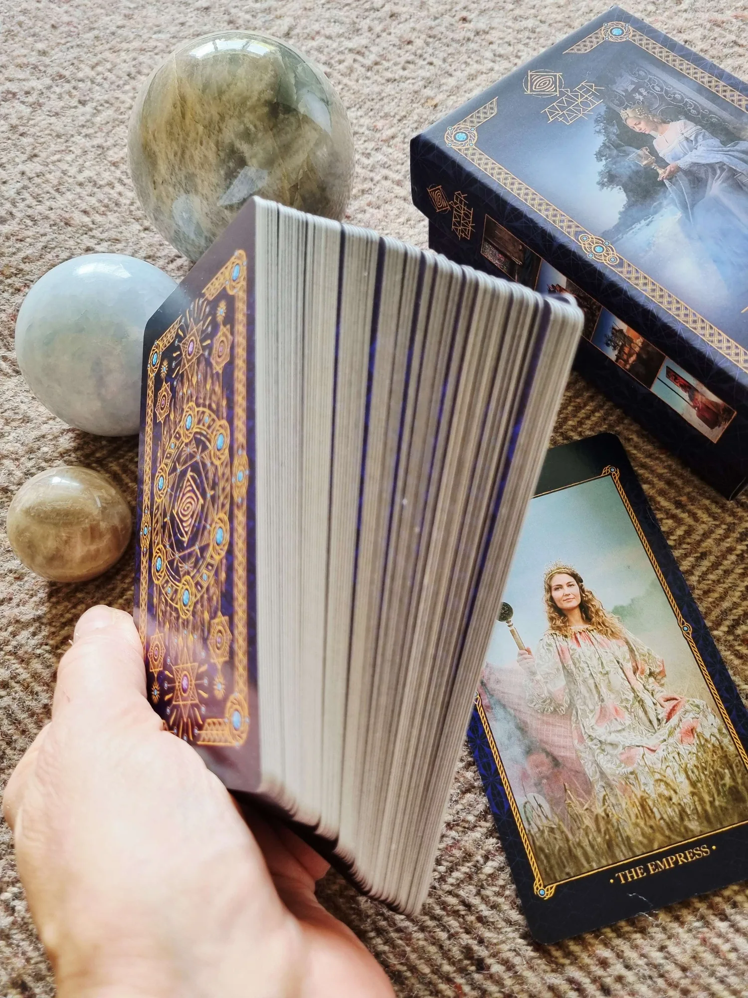 A hand holding the Amber Tarot deck on its side to show the thickness of the card stock, with The Empress card and the box behind
