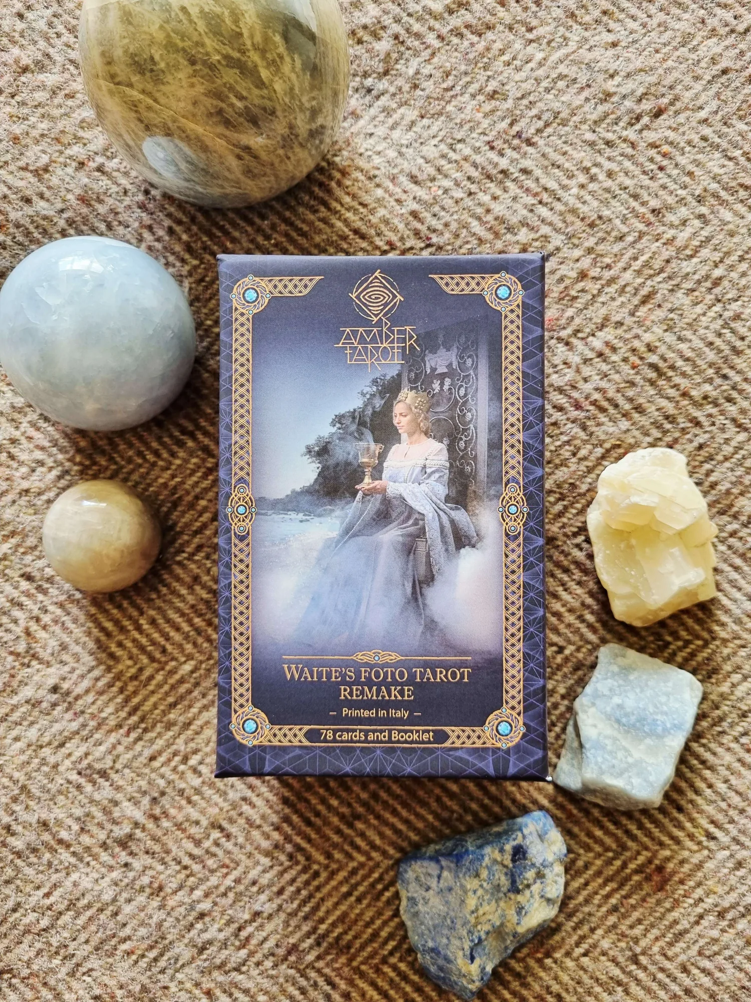 The front of the Amber Tarot box, Waite's Foto Tarot Remake, standing on woven matting among crystals and stone spheres