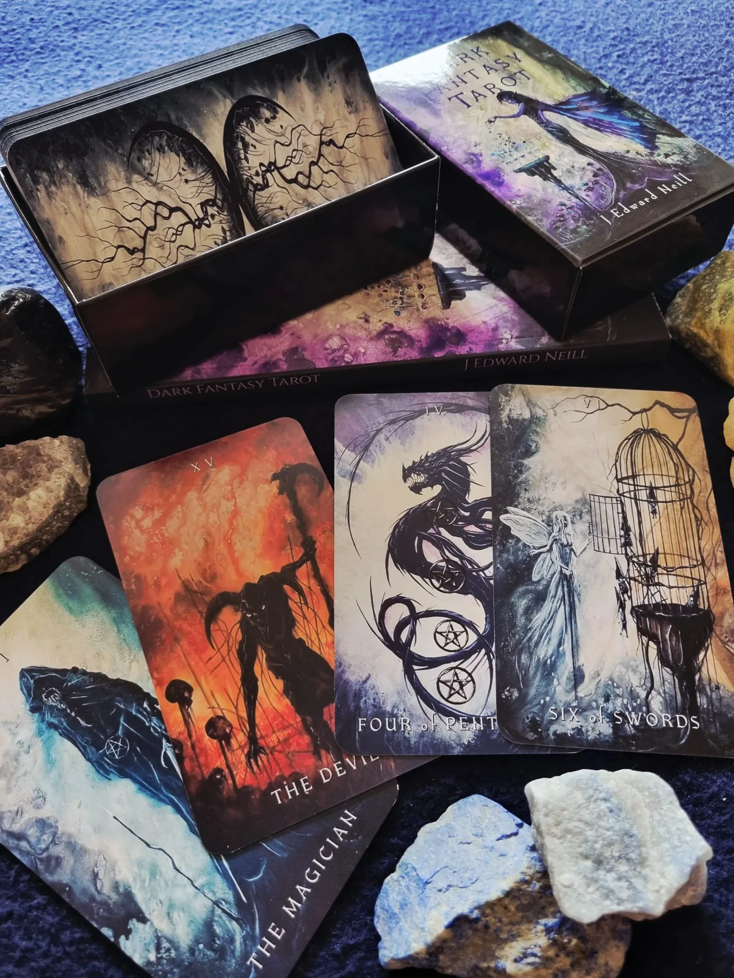 The Dark Fantasy Tarot deck in its black box with The Devil, Four of Pentacles, Six of Swords and The Magician spread in front on a deep blue cloth.