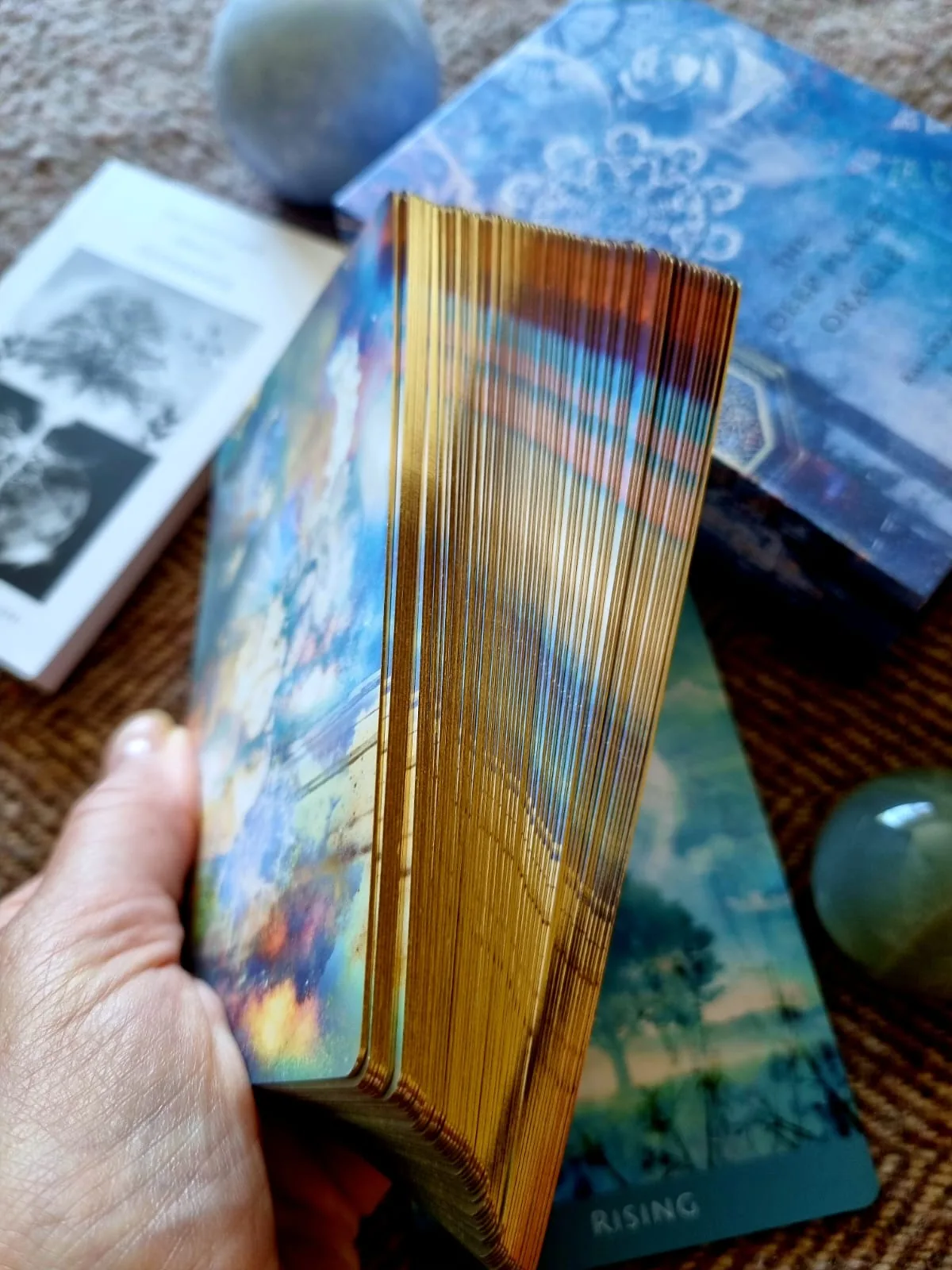 Hand holding the fanned Deep Place Oracle deck showing gilded edges