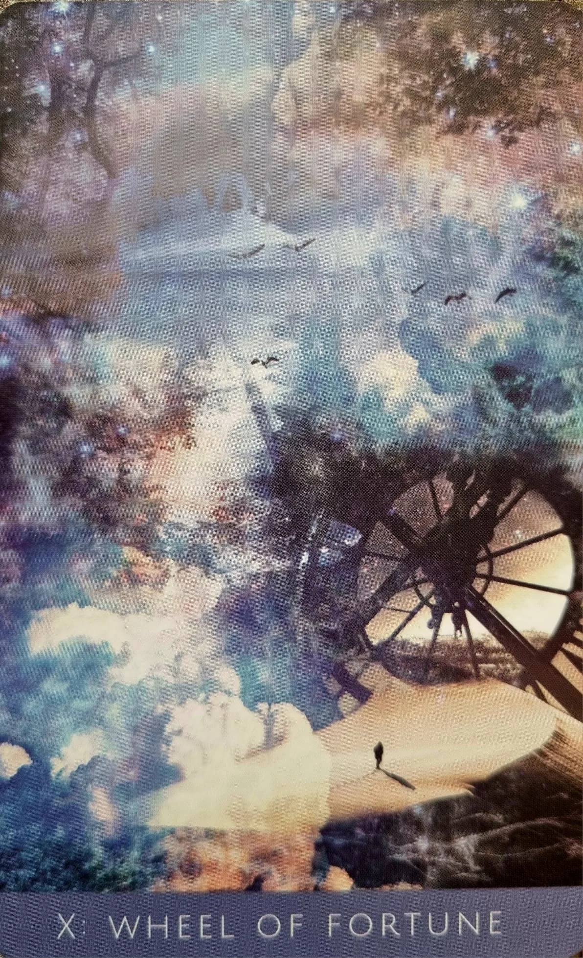 The Wheel of Fortune card from the Rooted Remembrance Tarot, a great wheel turning against a misty sky with birds in flight