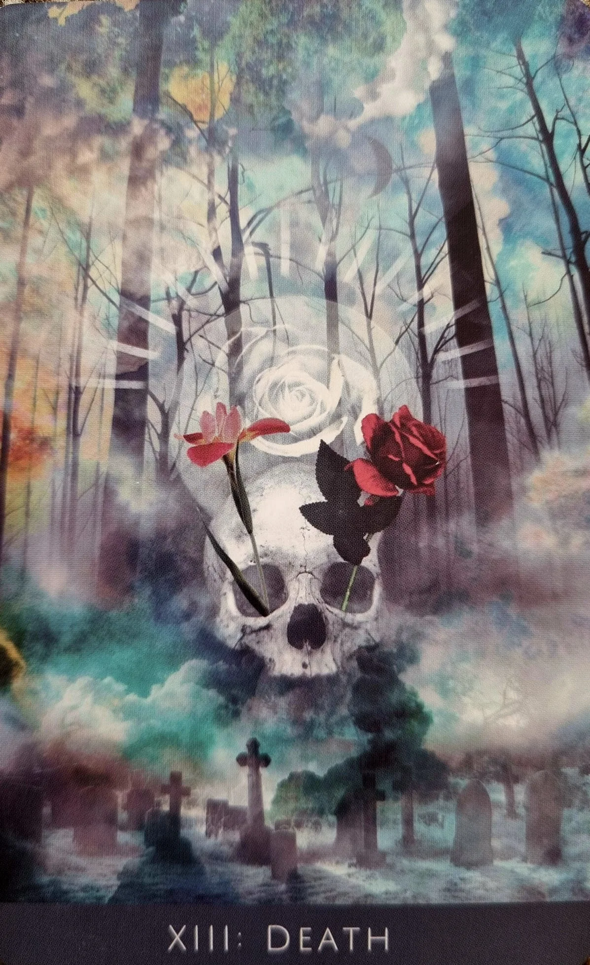 The Death card from the Rooted Remembrance Tarot, a skull wreathed in a white rose, red rose and gravestones in a misty forest