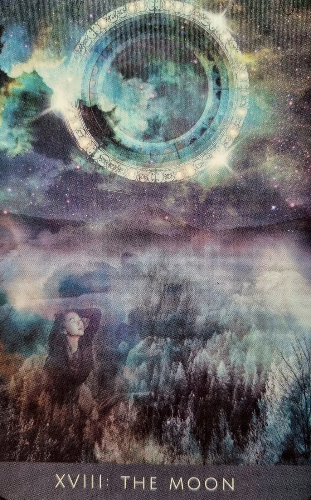 The Moon from the Rooted Remembrance Tarot, a figure reclining in long grass beneath a ringed moon in a starlit sky
