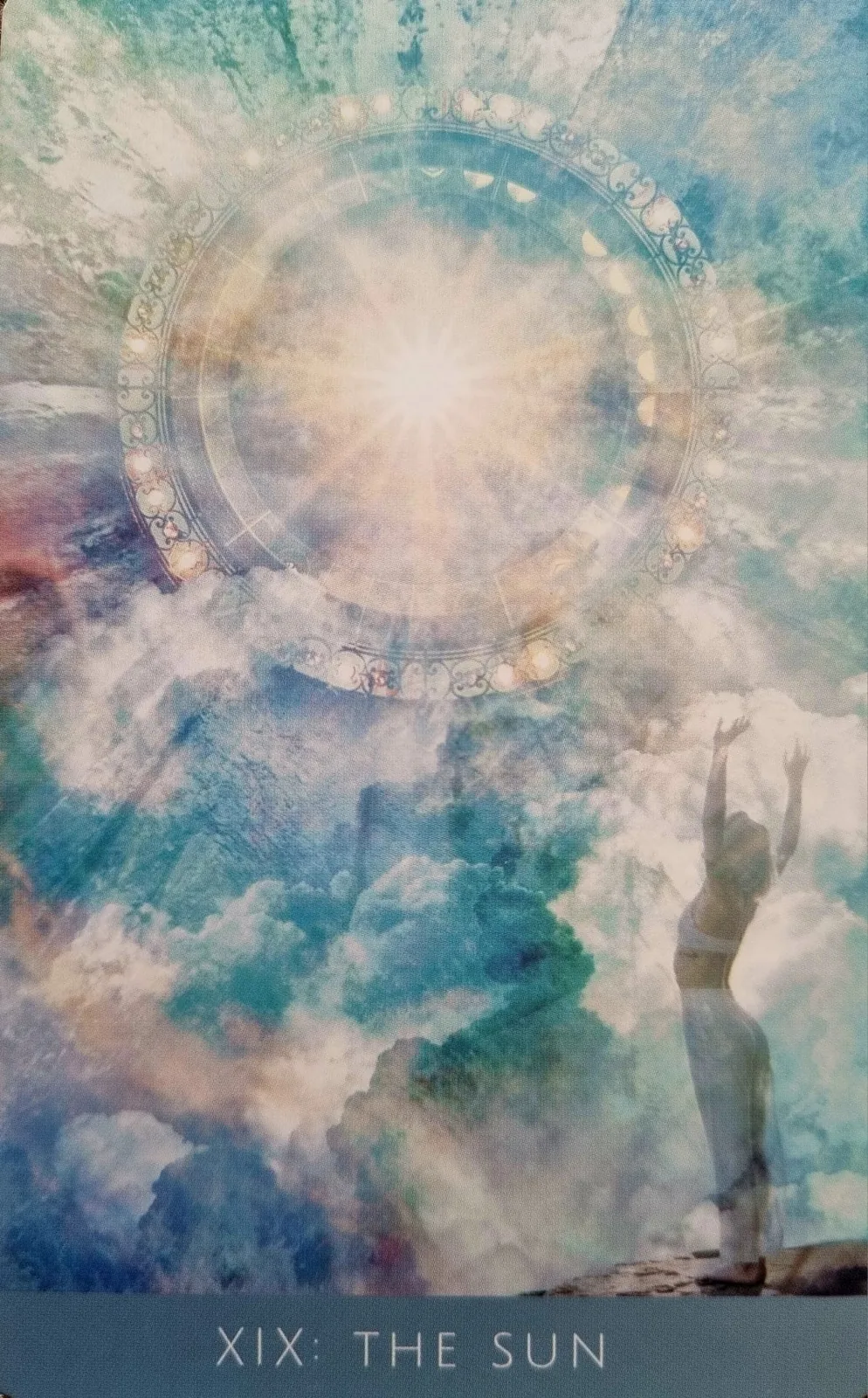 The Sun from the Rooted Remembrance Tarot, a figure reaching upward towards a radiant sun ringed with symbols above the clouds