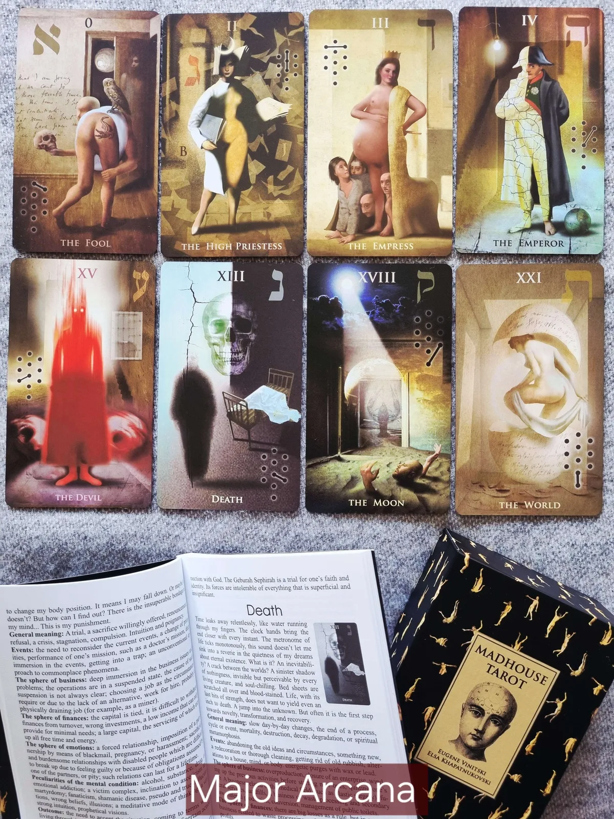 Major Arcana cards including The Fool, The Empress, The Devil, Death and The Moon beside an open Madhouse Tarot guidebook