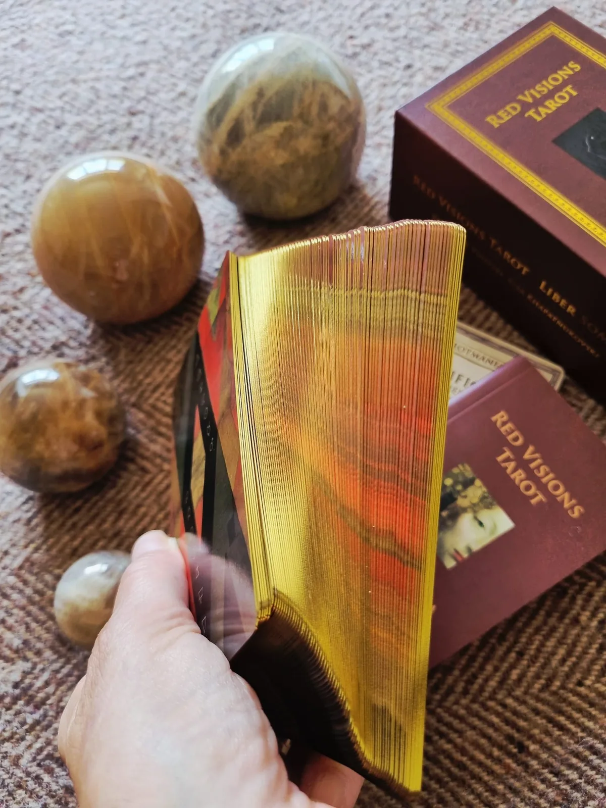 The gold gilded edges of Liber Somnia Red Visions Tarot fanned in the hand