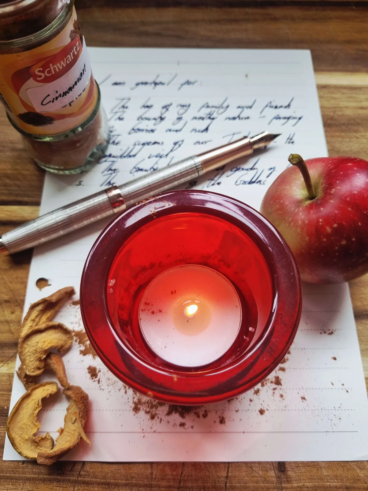 a red candle, an apple, cinnamon and a handwritten gratitude list for a Mabon spell