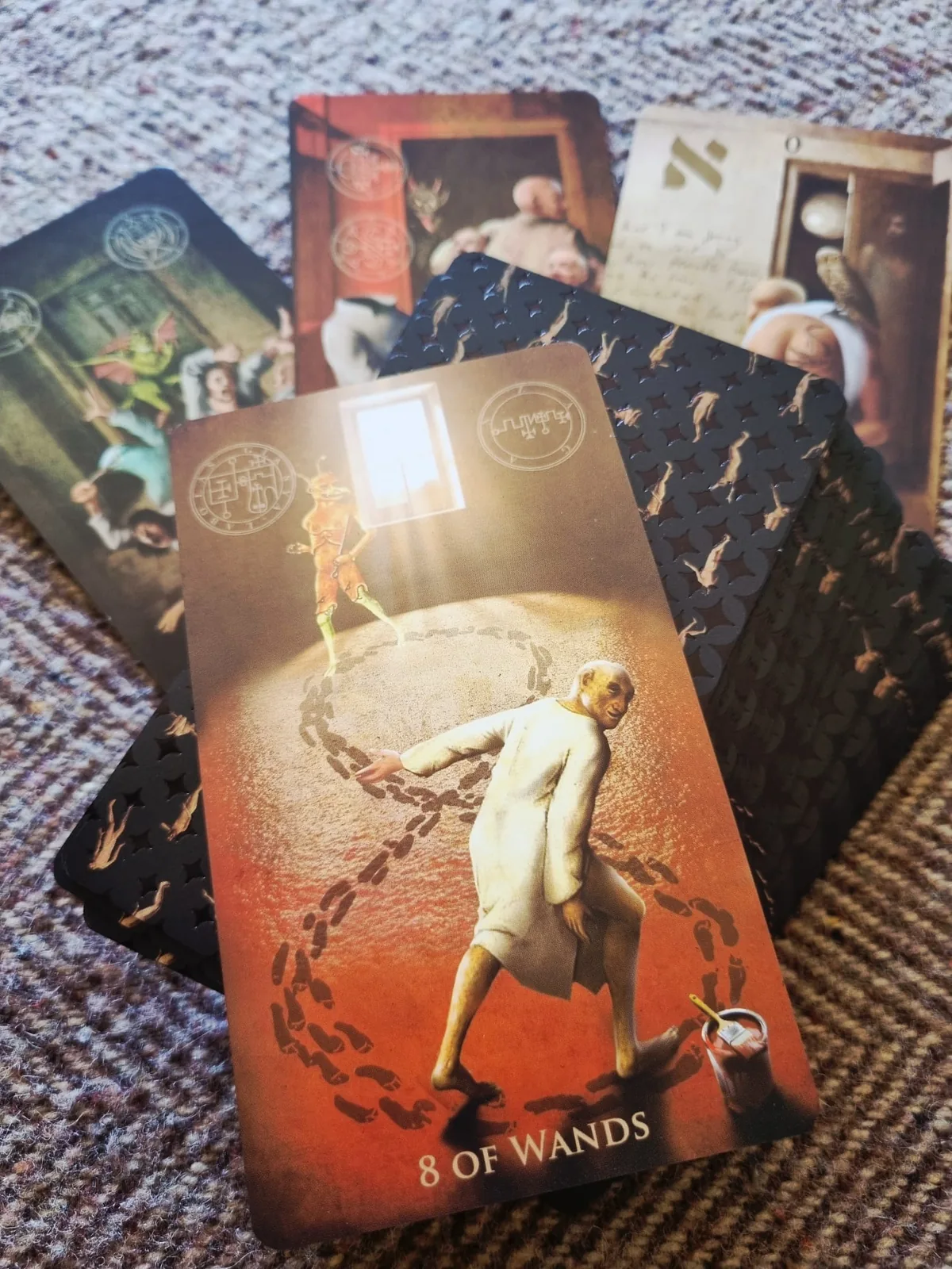 The Eight of Wands from The Madhouse Tarot, a figure dragging a chain in red and sepia tones