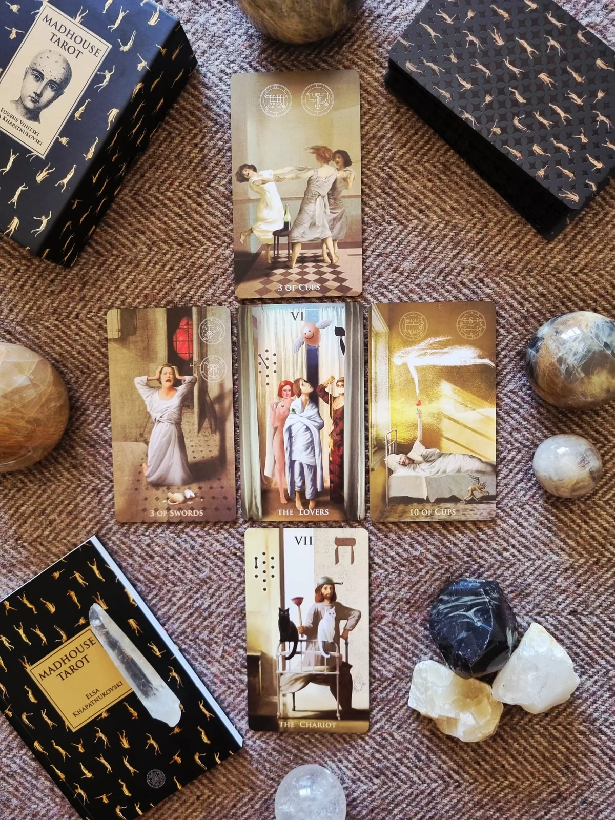 A spread of Madhouse Tarot cards with the deck box, quartz points and stone spheres