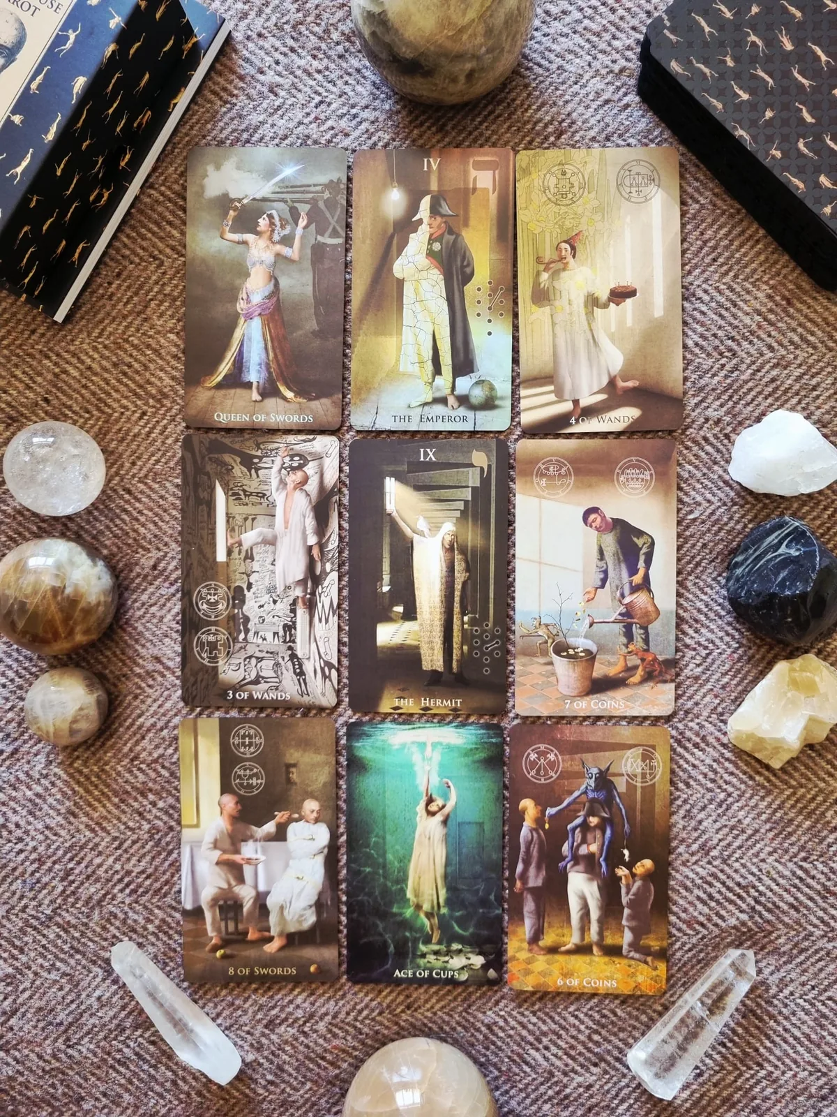 A grid of Madhouse Tarot cards laid out with crystals on a woven cloth