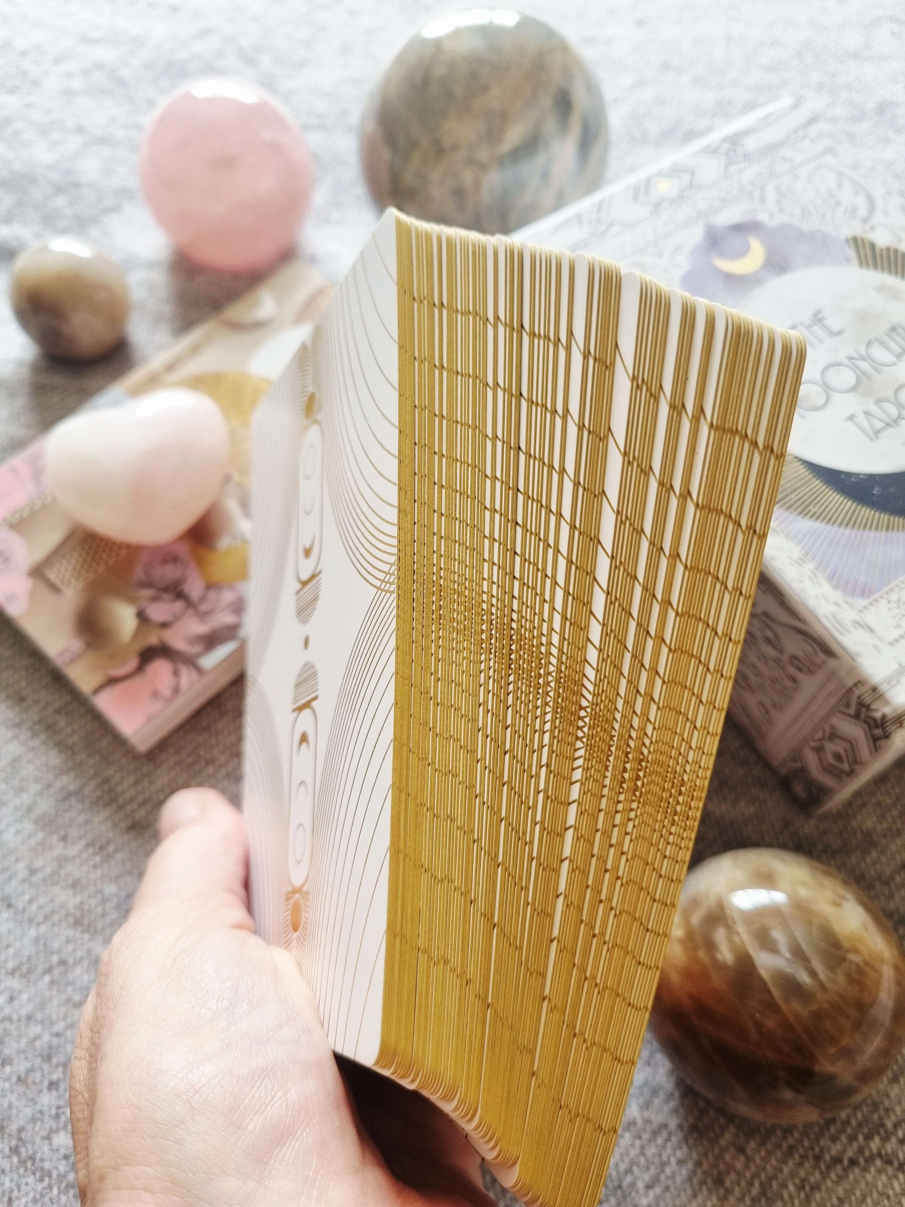 a hand fanning the Moonchild Tarot White and Gold Edition deck to show its gold gilded edges