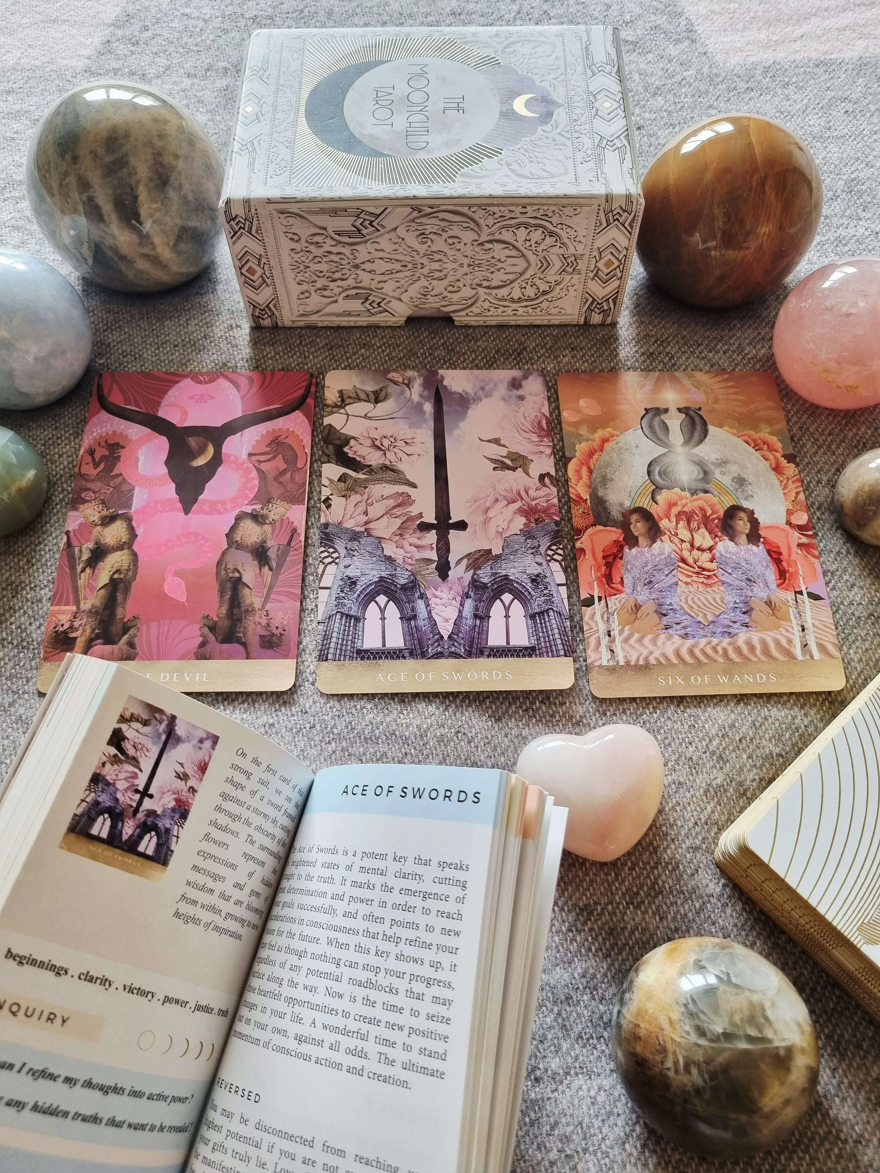 The Moonchild Tarot White and Gold Edition box, guidebook and deck beside The Devil, Ace of Swords and Six of Wands cards