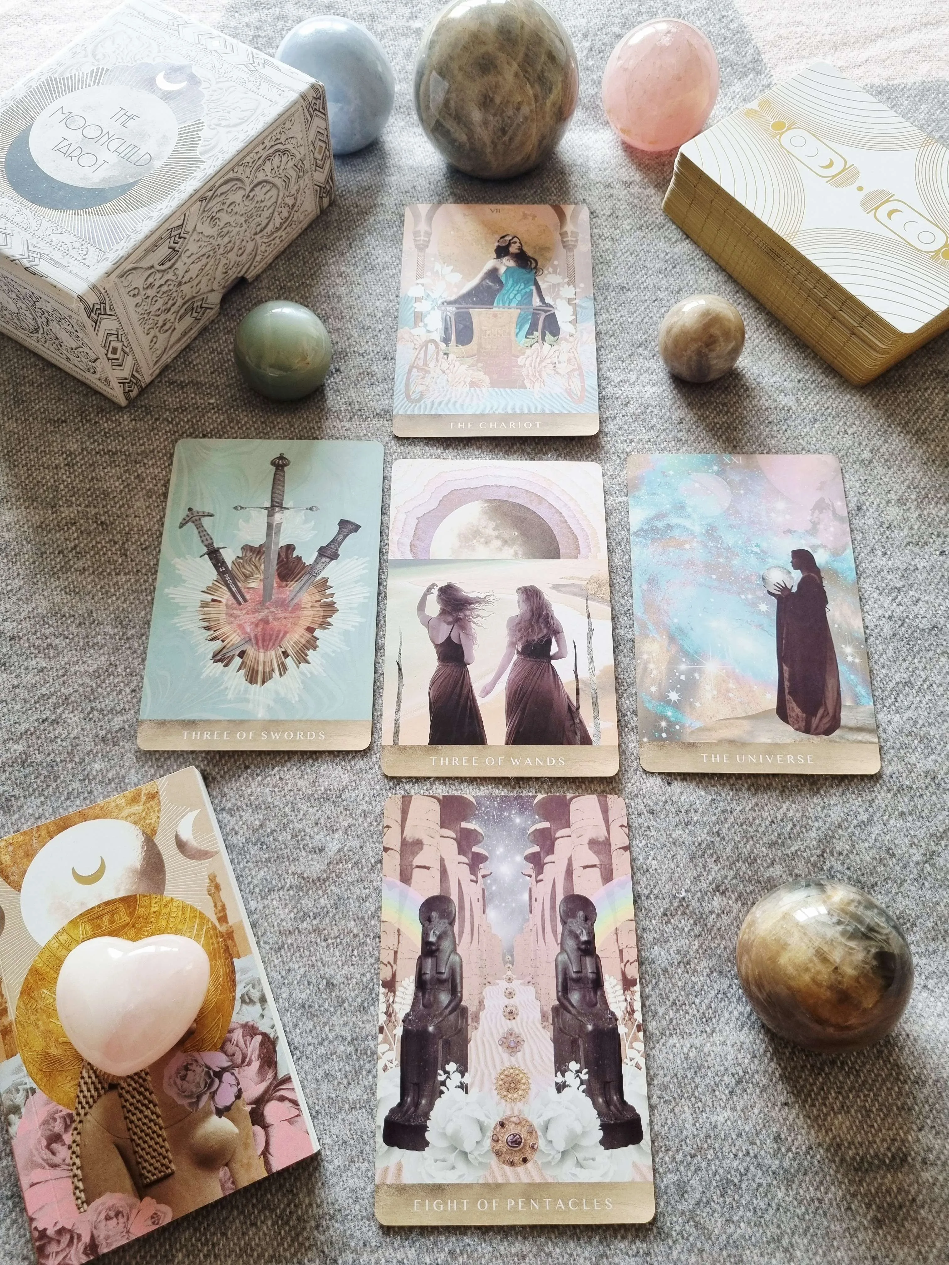 The Moonchild Tarot White and Gold Edition box beside The Chariot, Three of Swords, Three of Wands, The Universe and Eight of Pentacles cards
