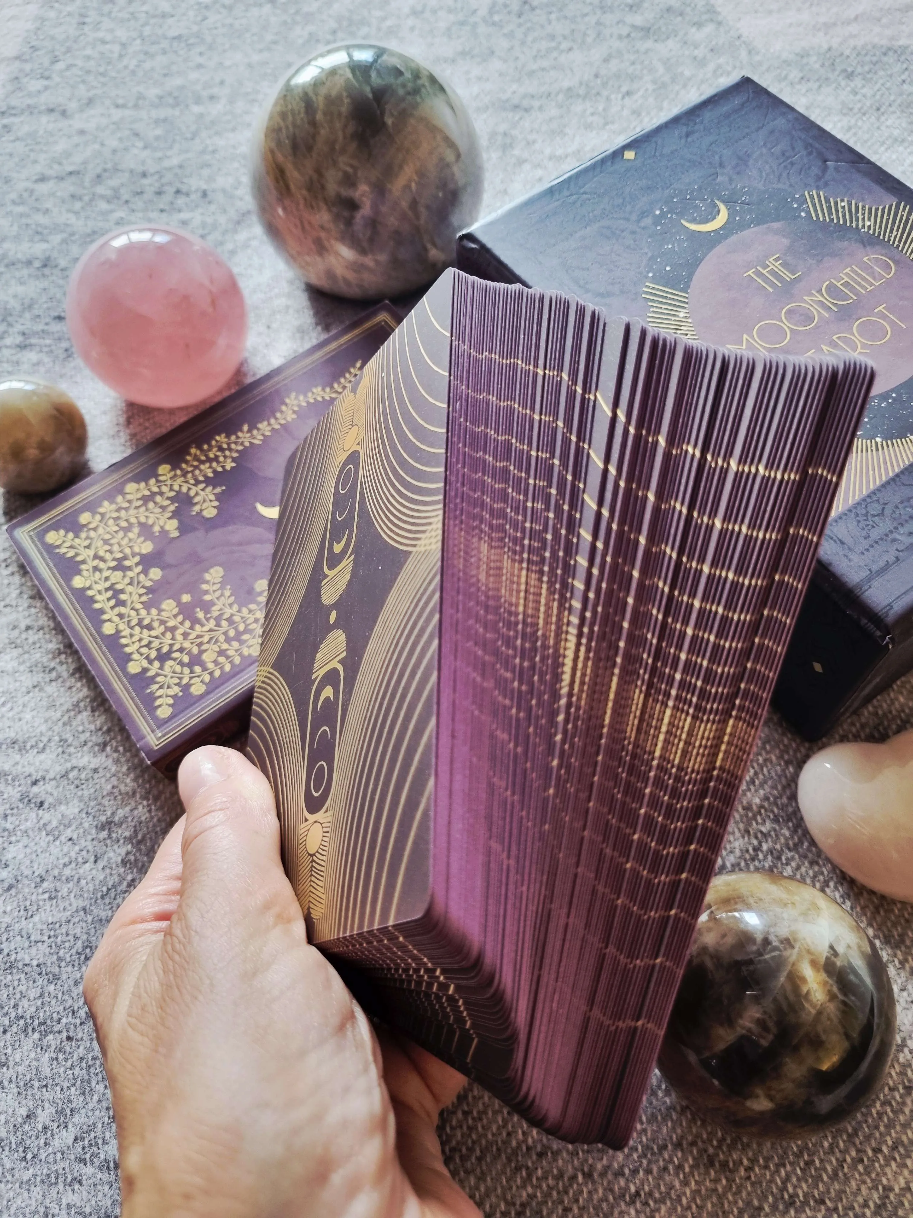 a hand fanning the Moonchild Tarot Shadow Work Edition deck to show its aubergine and gold card backs