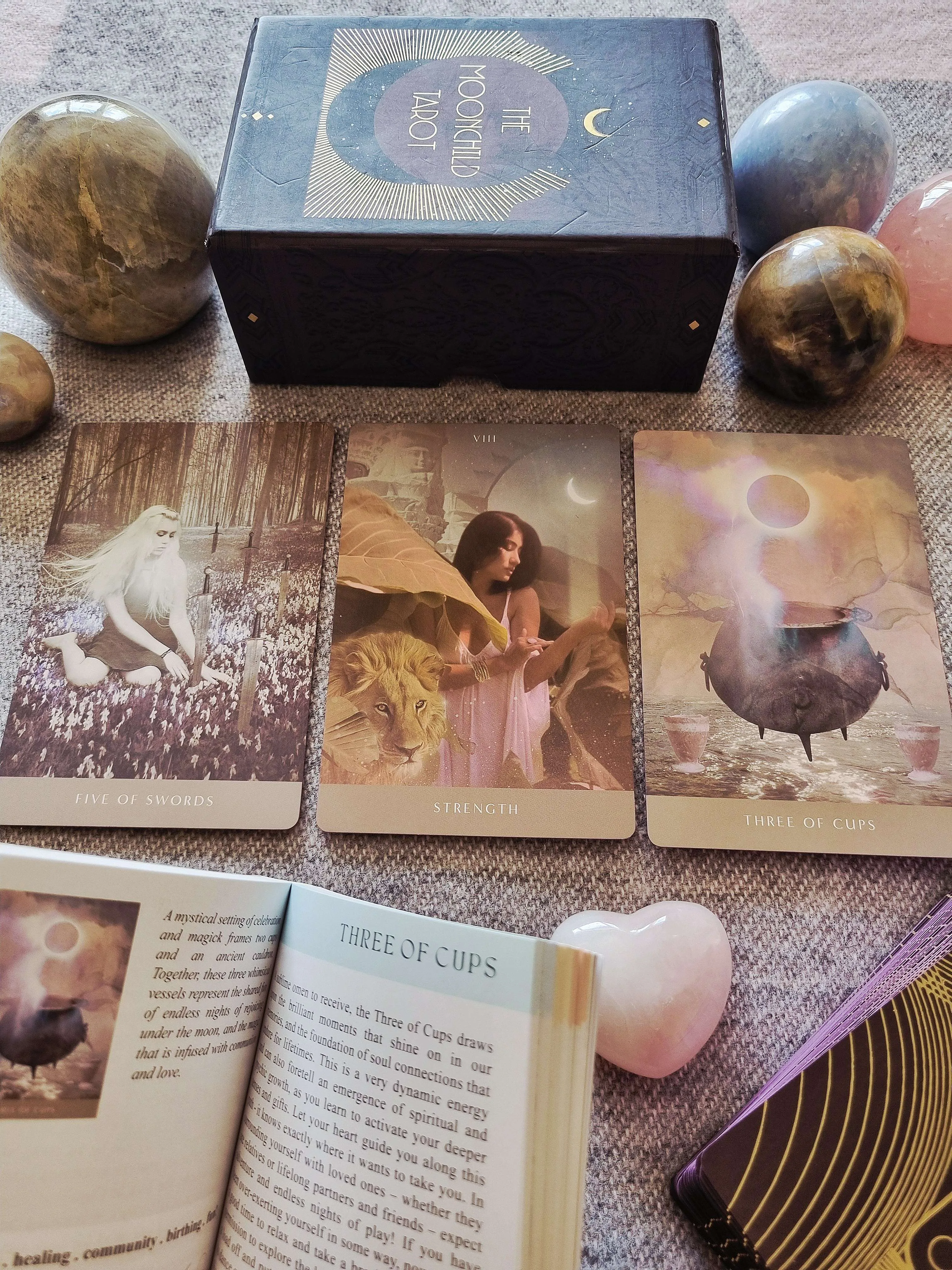 The Moonchild Tarot Shadow Work Edition box, guidebook and deck beside Five of Swords, Strength and Three of Cups cards