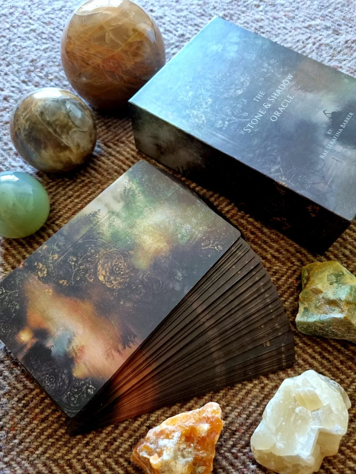 Hand holding the fanned Stone and Shadow Oracle deck showing gold gilded edges