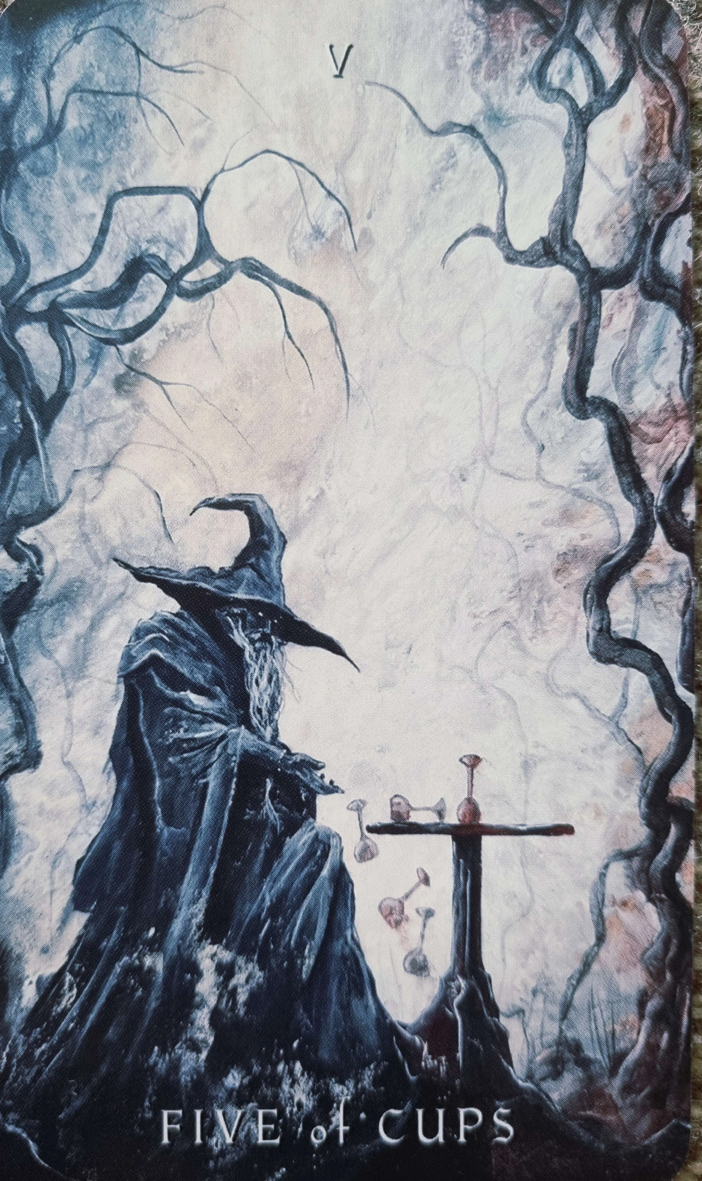 Five of Cups tarot card, a hooded figure seated before spilled and standing cups
