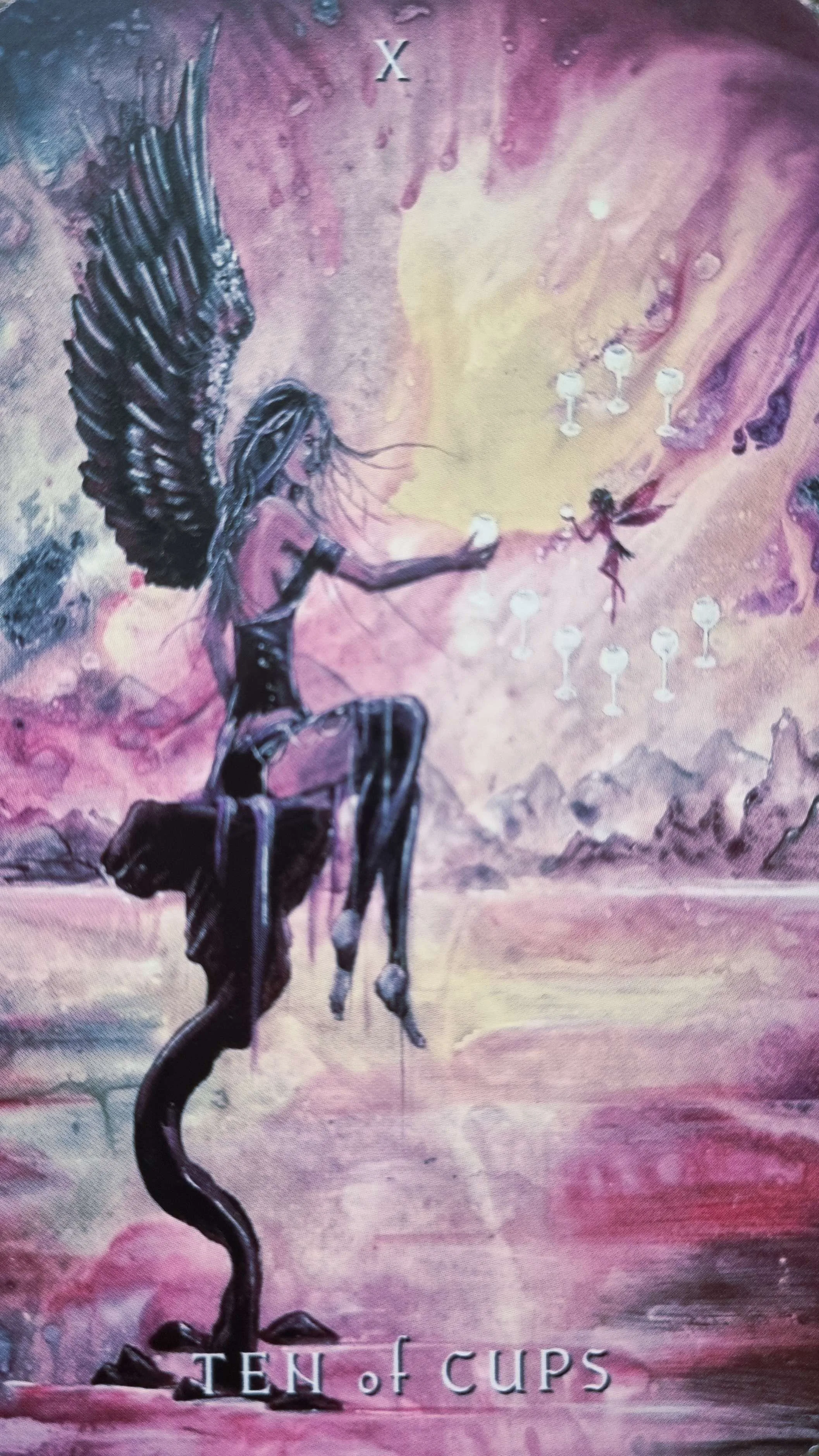 Ten of Cups tarot card, a winged figure offering a cup towards a fairy amid a rainbow of cups