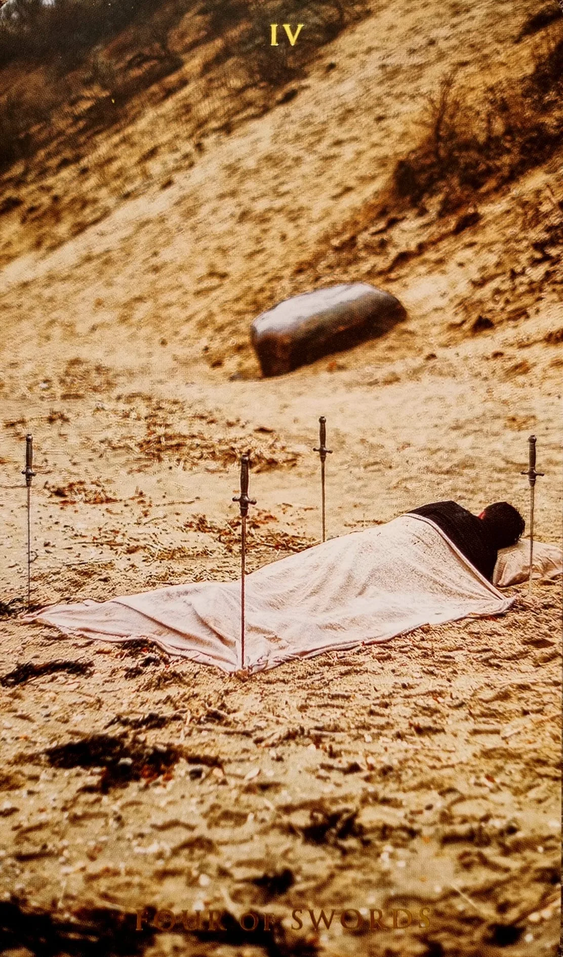 Four of Swords card: a cloaked figure resting beneath four swords planted in the sand