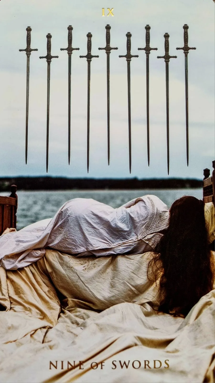 Nine of Swords card: a figure lying awake in bed beneath nine suspended swords at dawn