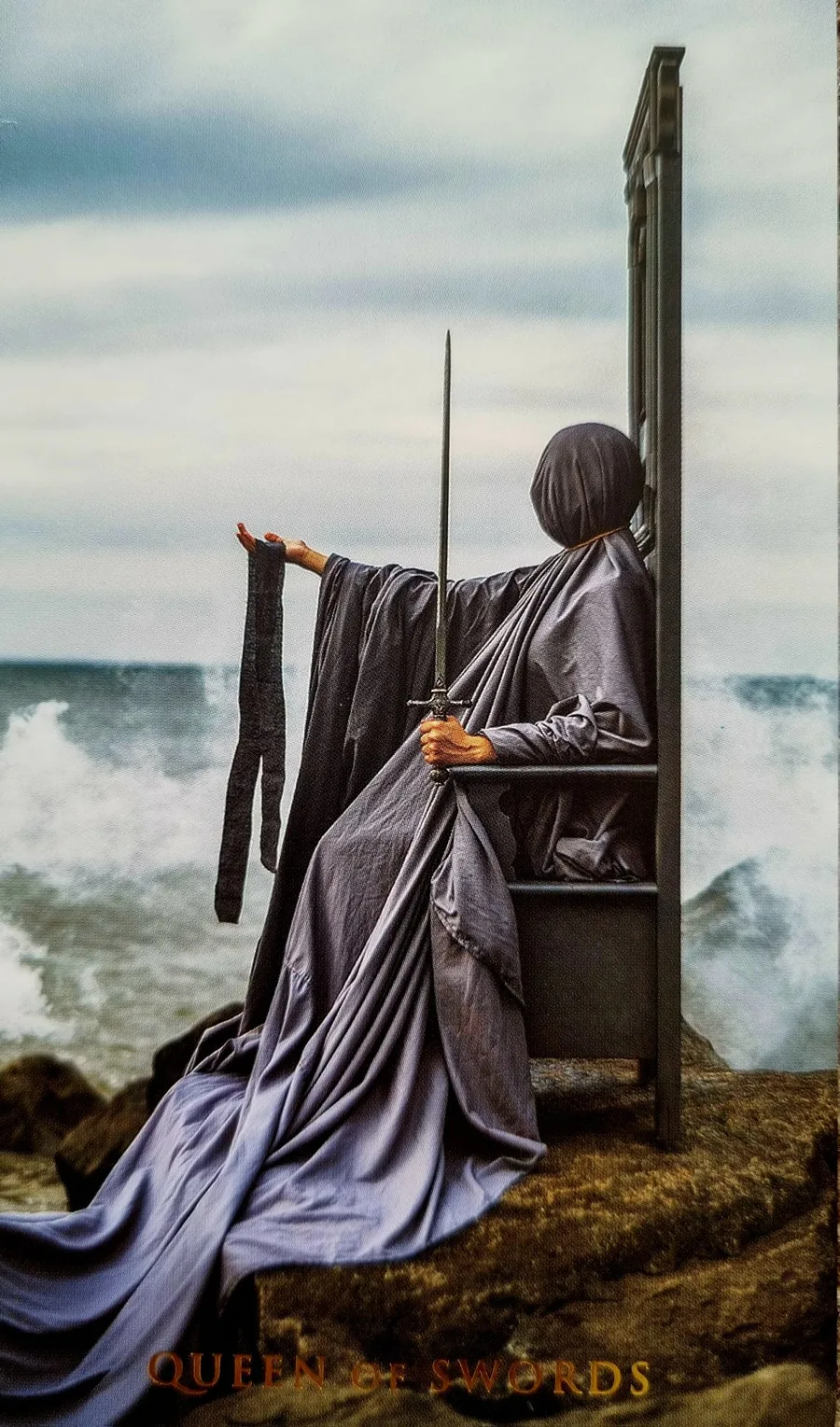 Queen of Swords card: a veiled figure enthroned above crashing waves holding an upright sword