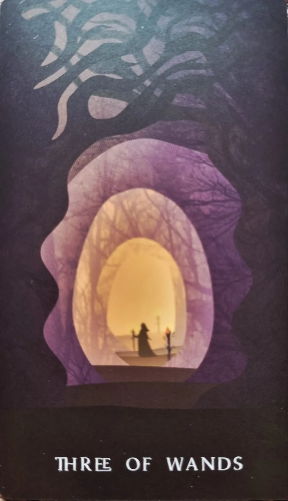 Three of Wands tarot card, a figure looking out through a layered archway