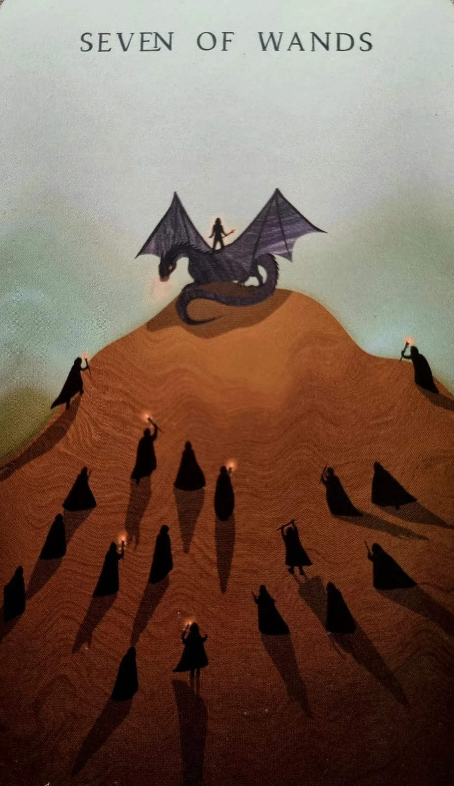 Seven of Wands tarot card, a dragon rider on a hilltop above a crowd of figures