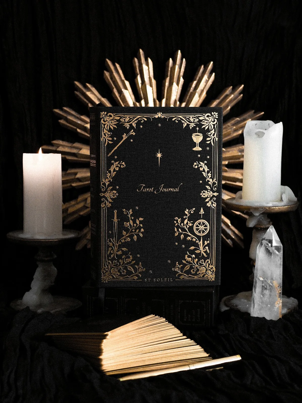 St Soleil Tarot Journal in black linen with gold foil, between candles and a quartz crystal