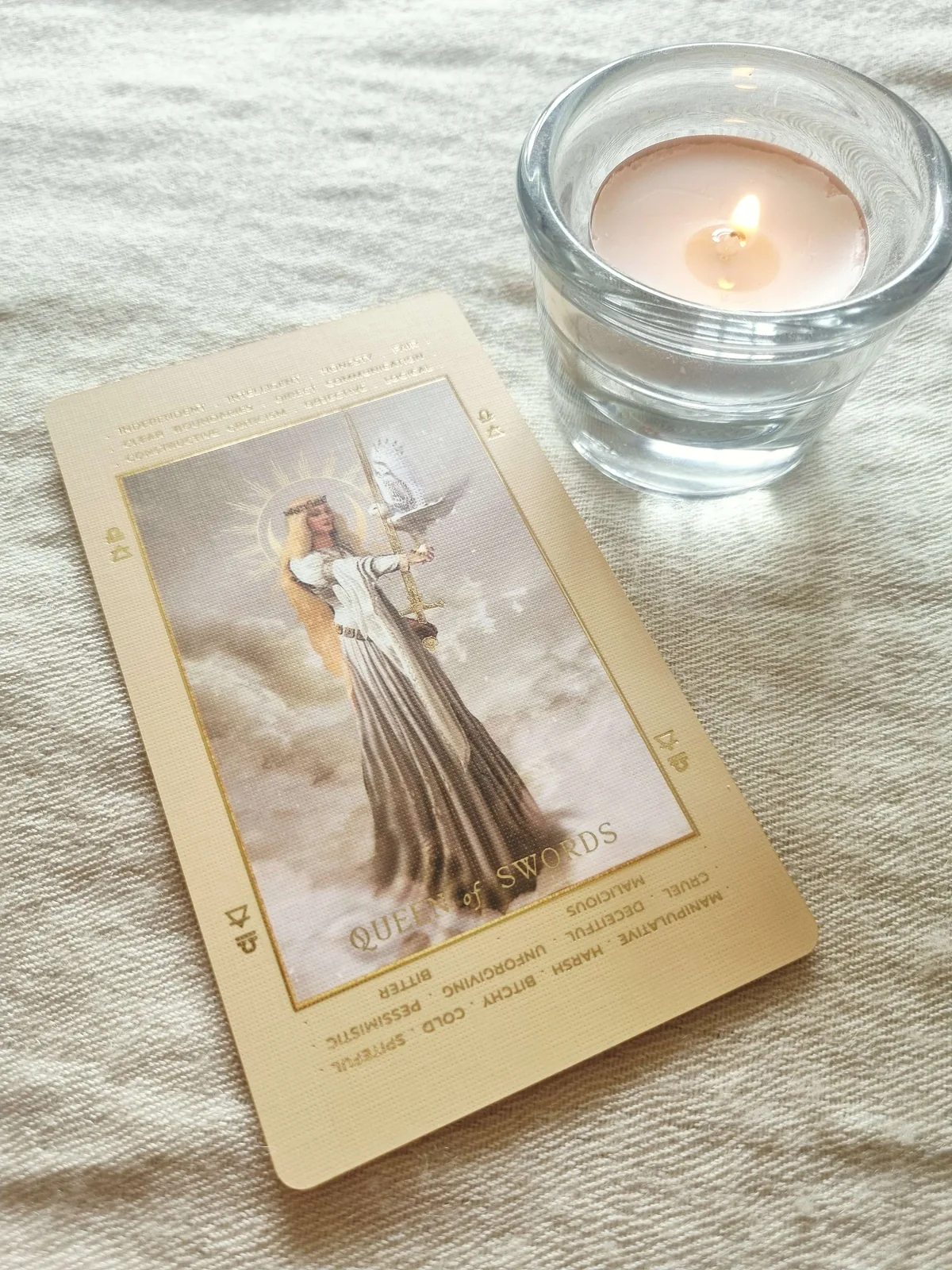 Queen of Swords tarot card beside a lit candle in a glass holder