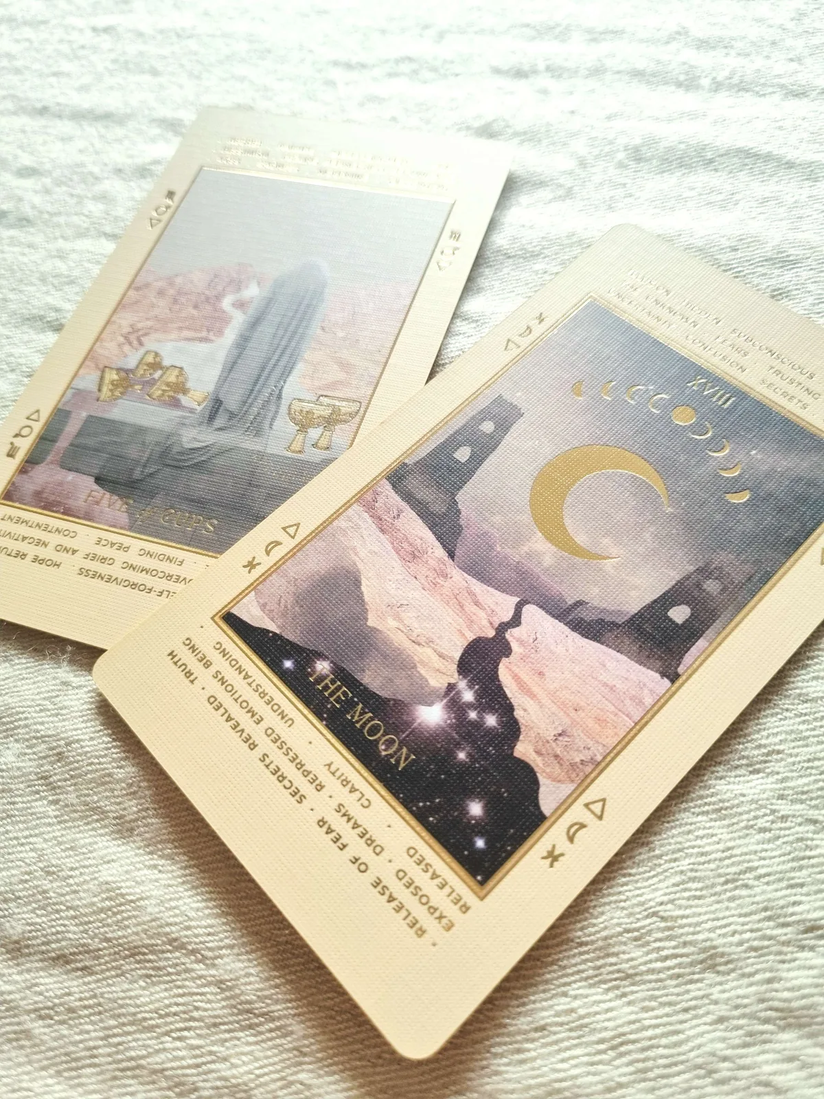 Five of Cups and The Moon tarot cards on linen